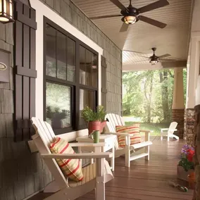 A front porch with wood flooring, shingled siding and white columns with stone details includes PlyGem windows with dark trim.