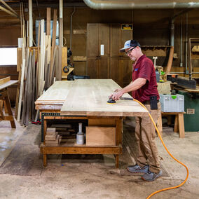 An employee of a custom woodworking and millwork shop sands a piece of wood for a customer