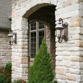 Image of arched stone entry way to home with porch lights and evergreen shrubbery