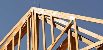 Pictured is a pair of wood trusses hoisted against a clear blue sky before being placed.